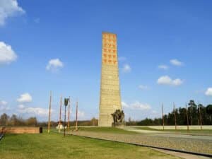 Hohes Denkmal mit orangefarbenen Symbolen und Skulpturen im Vordergrund auf einer Wiese.