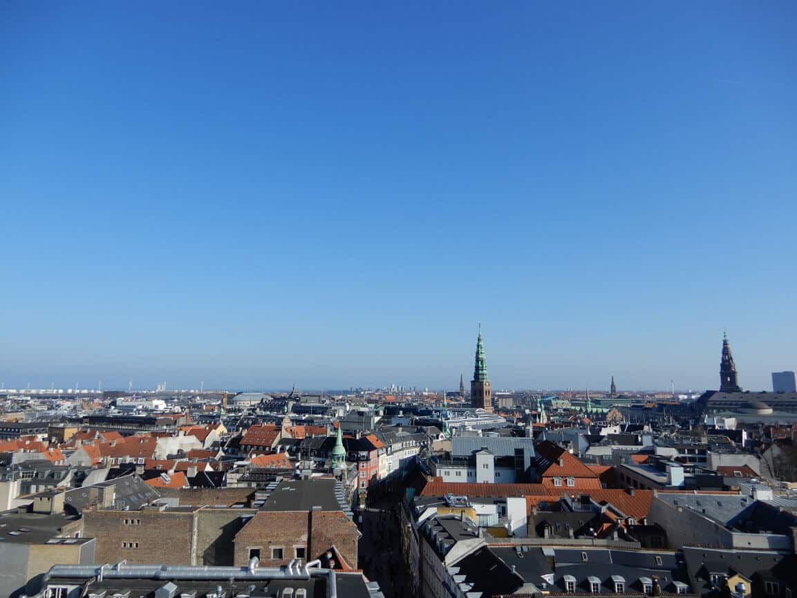Blick auf eine Kopennhagen mit roten Dächern und mehreren Kirchtürmen unter blauem Himmel.
