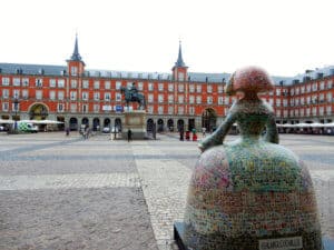 Bunte Skulptur einer Frau mit einer großen Rockform auf dem Platz in Madrid, mit einem Reiterdenkmal im Hintergrund.