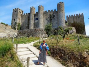 Eine Frau in einem gestreiften Kleid steht vor einer steinernen Burg mit Türmen und Mauern.