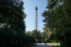 Ein hoher Fernsehturm steht in einem Park, umgeben von Bäumen und Grünflächen.
