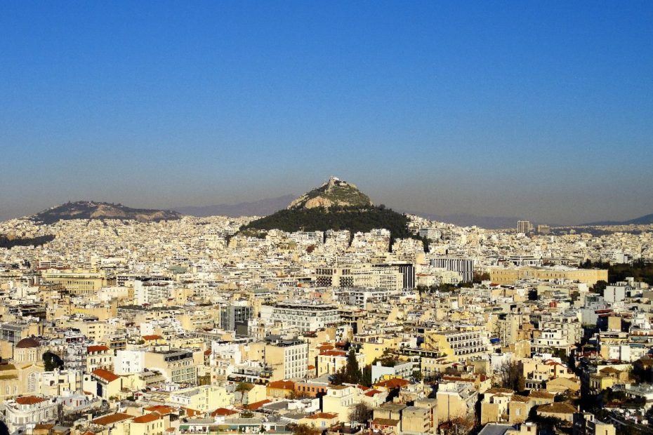 Blick auf die Stadt Athen mit einem Hügel im Hintergrund und zahlreichen Gebäuden im Vordergrund.