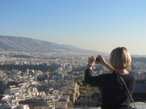 Frau mit blonden Haaren macht ein Foto von der Stadt Athen mit einer Kamera.
