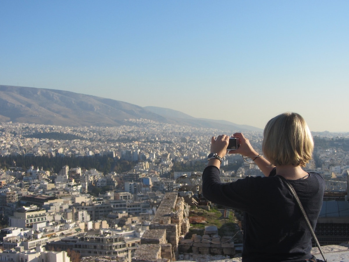 Frau mit blonden Haaren macht ein Foto von der Stadt Athen mit einer Kamera.