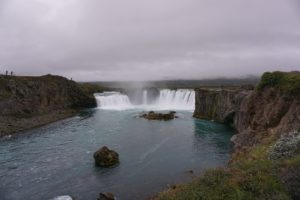 Godafoss Wasserfall mit Wasser, das über die Felsen fließt, umgeben von grünem Gelände.