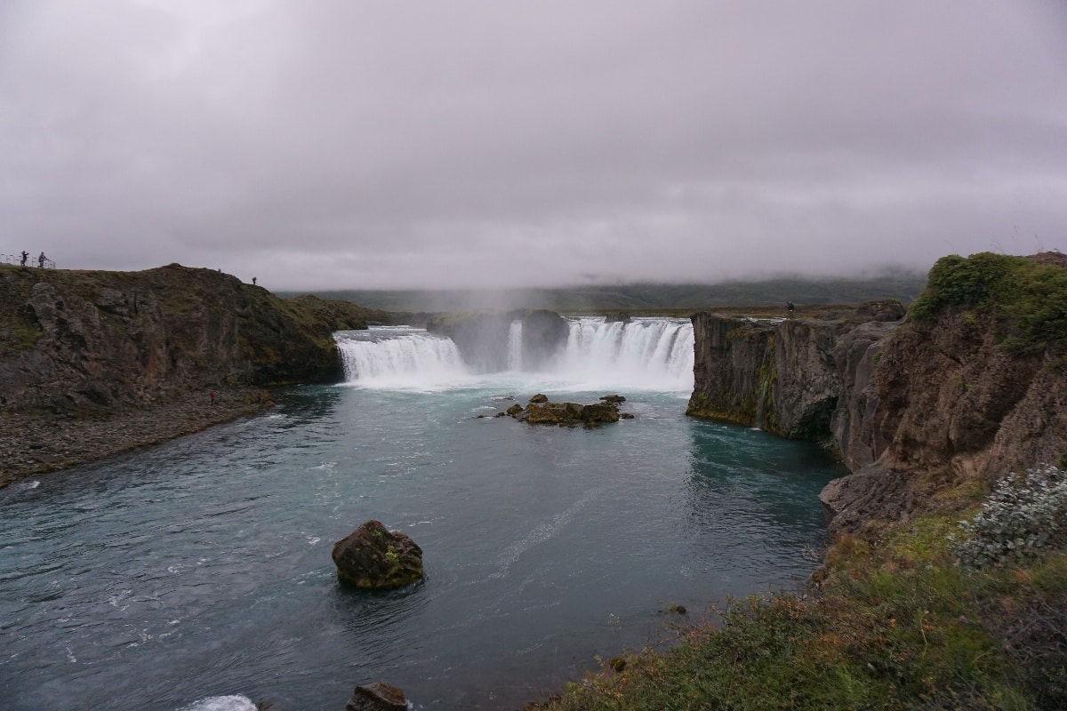 Godafoss Wasserfall mit Wasser, das über die Felsen fließt, umgeben von grünem Gelände.