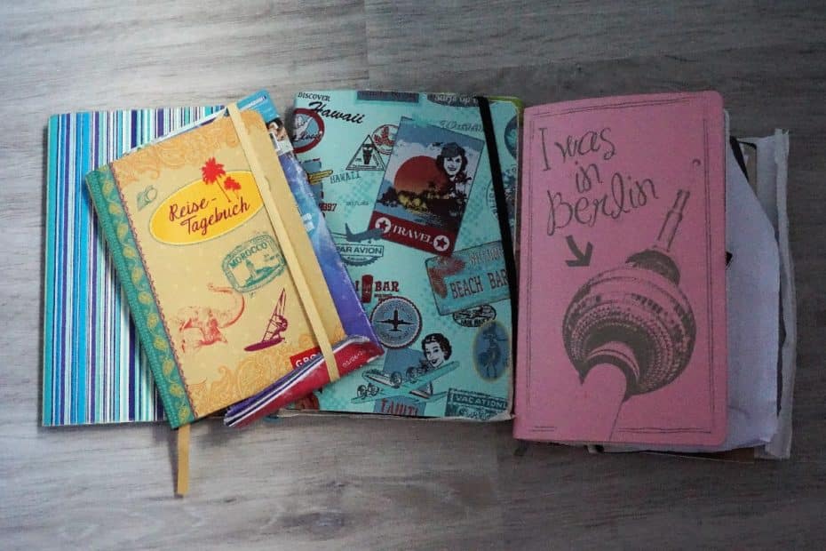 Drei Notizbücher in verschiedenen Designs, darunter ein Reisetagebuch und ein pinkes Notizbuch mit Berliner Motiv.