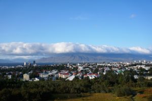 Blick auf die Stadt Reykjavik mit bunten Dächern und Bergen im Hintergrund unter einem bewölkten Himmel.