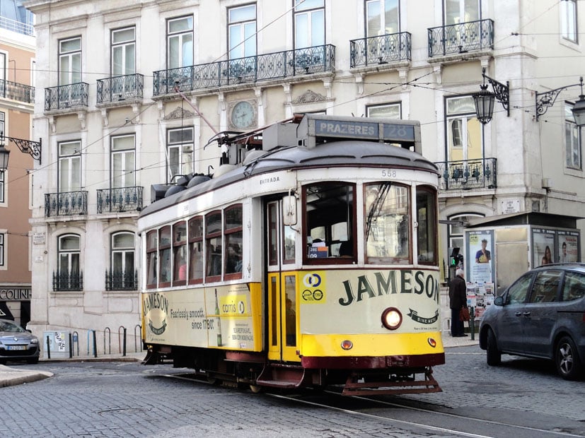 Eine Straßenbahn mit der Aufschrift 'Jameson' fährt durch eine Straße in Lissabon.