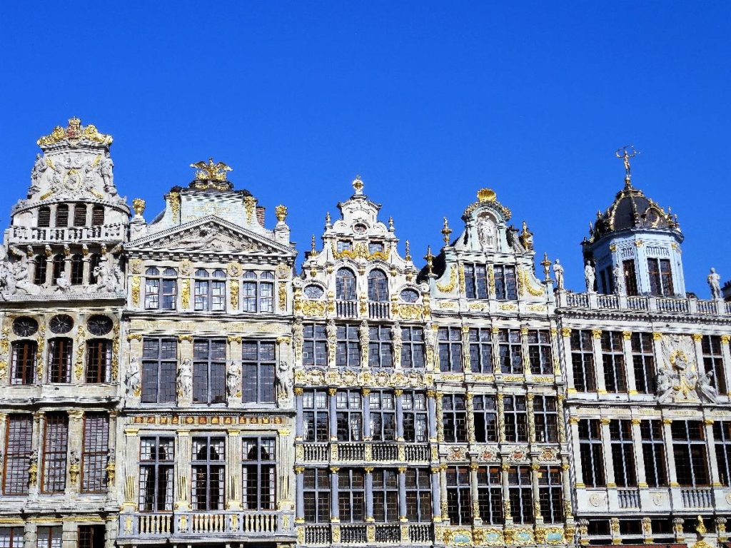 Historische Gebäude mit aufwendiger Fassade und goldenen Verzierungen in Brüssel unter blauem Himmel.