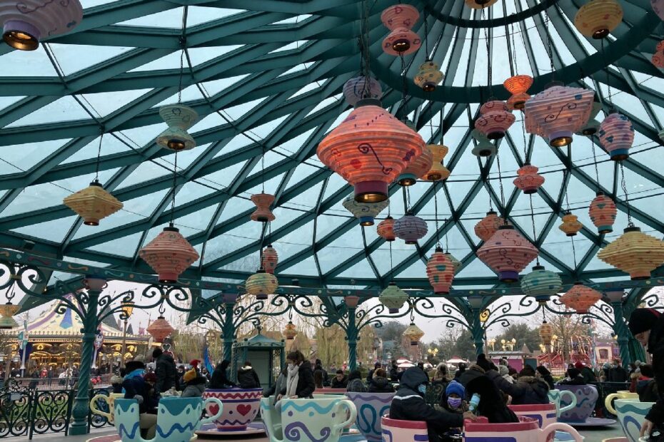 Bunte Teetassenfahrt mit großen, dekorativen Lampen und Besuchern im Vergnügungspark.