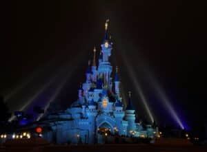 Beleuchtetes Schloss im Disneyland Paris mit bunten Lichtern und Nebel bei Nacht.