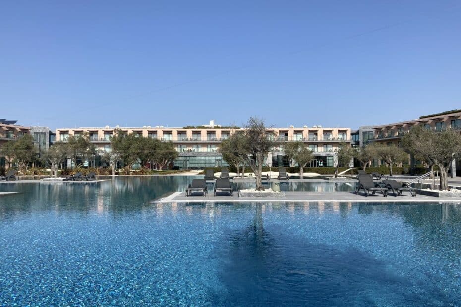 Ein Hotel mit einem großen Pool und Liegen umgeben von Bäumen und Gebäuden.
