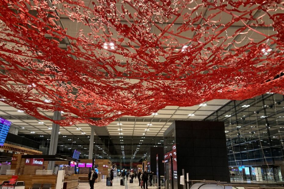 Rote Kunstinstallation aus Zweigen hängt von der Decke in einem modernen Flughafenbereich.