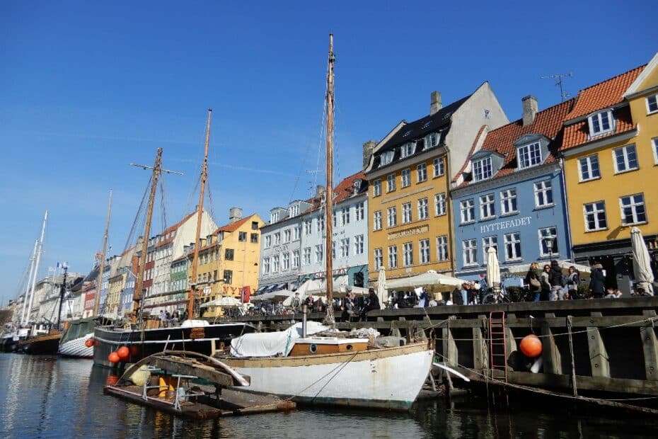 Bunte Häuser und Boote am Hafen von Kopenhagen unter blauem Himmel.