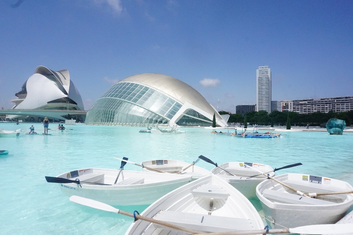 Mehrere kleine Boote im Wasser mit moderner Architektur im Hintergrund, darunter ein gewölbtes Gebäude.