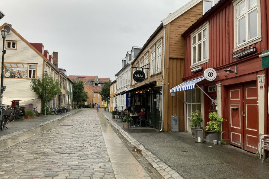 Eine gepflasterte Straße mit historischen Holzhäusern und einem Restaurant in Norwegen.