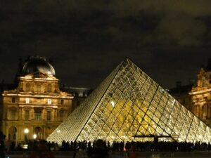 Glaspyramide des Louvre-Museums beleuchtet bei Nacht mit Menschen im Vordergrund.