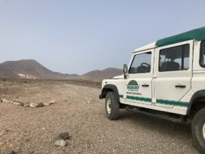 Weißer Land Rover Discovery mit grünem Dach auf einer unbefestigten Straße in einer bergigen Landschaft.