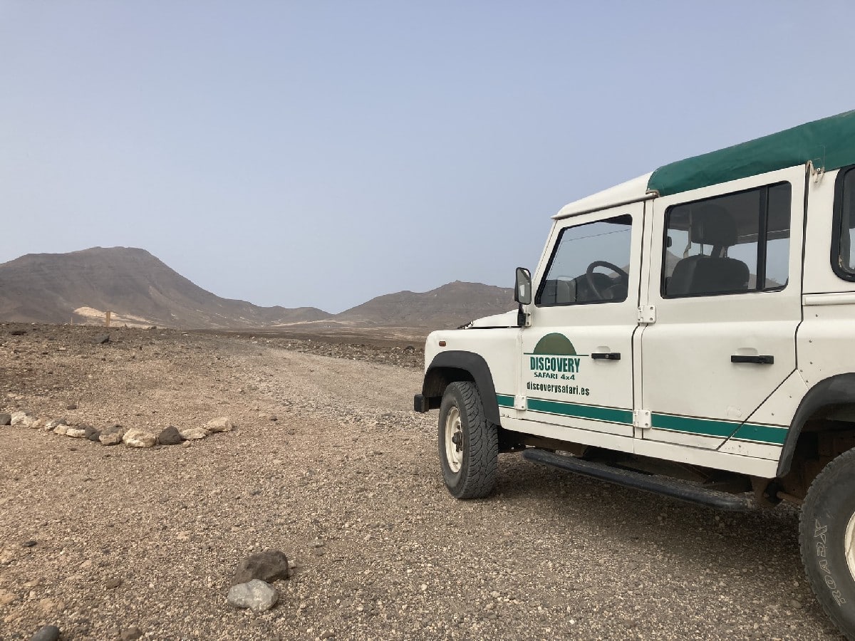 Weißer Land Rover Discovery mit grünem Dach auf einer unbefestigten Straße in einer bergigen Landschaft.