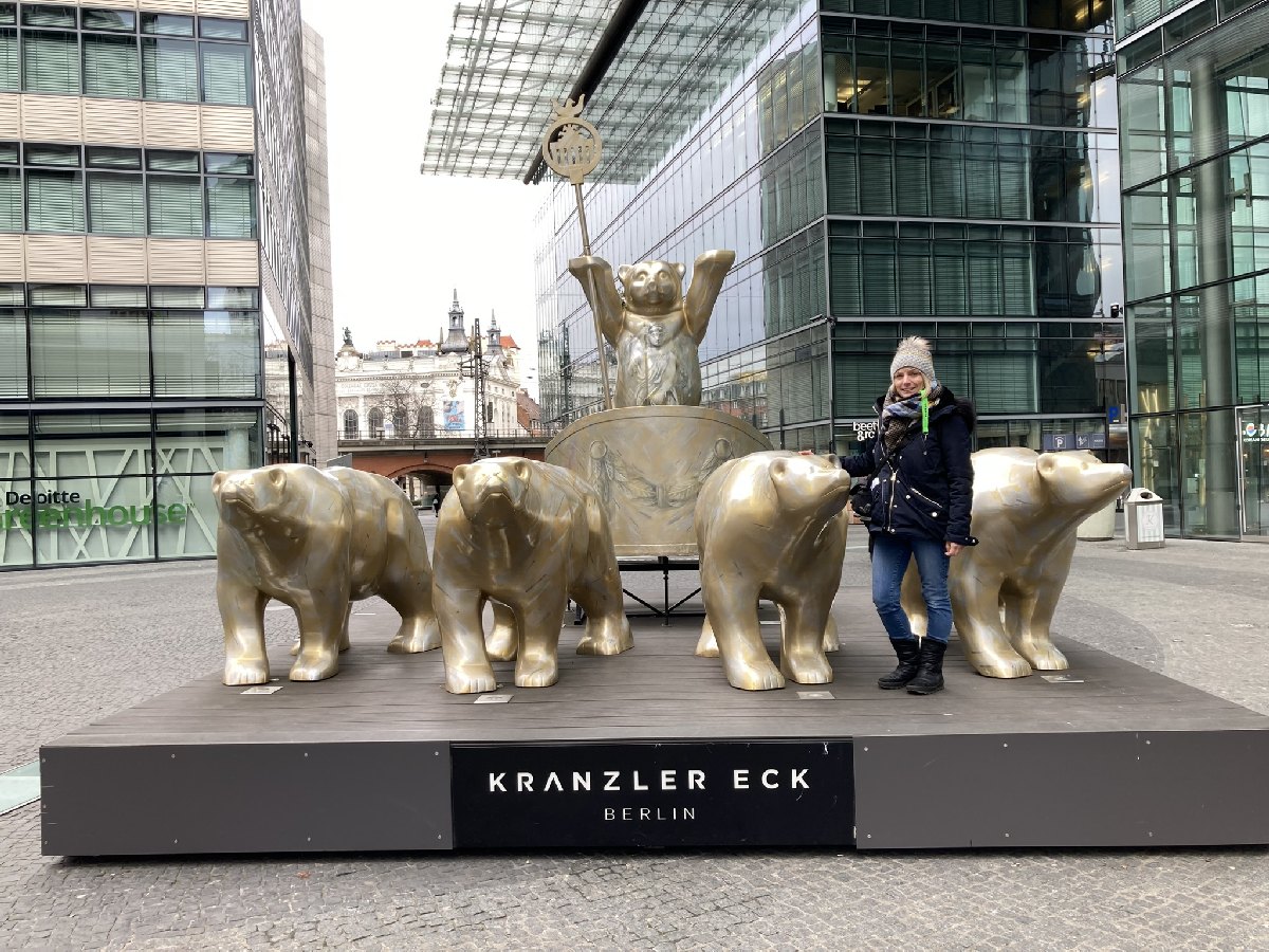 Eine Person steht neben einer Skulptur mit goldenen Bären und einem Bären, der auf einem Podest steht, in Berlin.