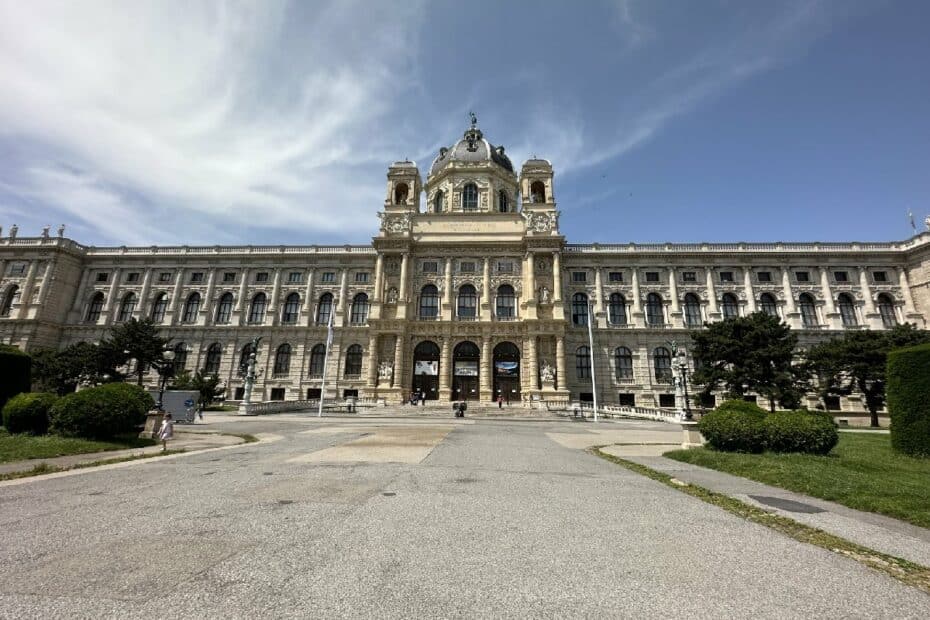 Historisches Gebäude mit einer großen Fassade und einem zentralen Eingangsbereich, umgeben von Bäumen und Rasenflächen.