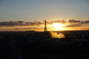 Eiffelturm in Paris vor einem Sonnenuntergang mit Wolken und Lichtreflexionen.