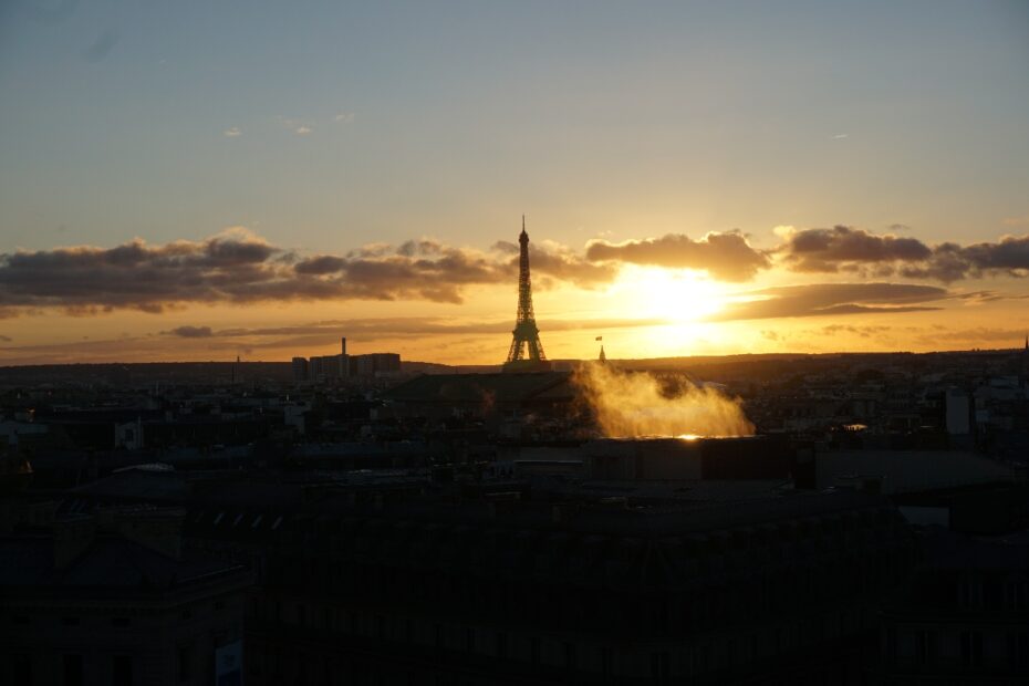 Eiffelturm in Paris vor einem Sonnenuntergang mit Wolken und Lichtreflexionen.
