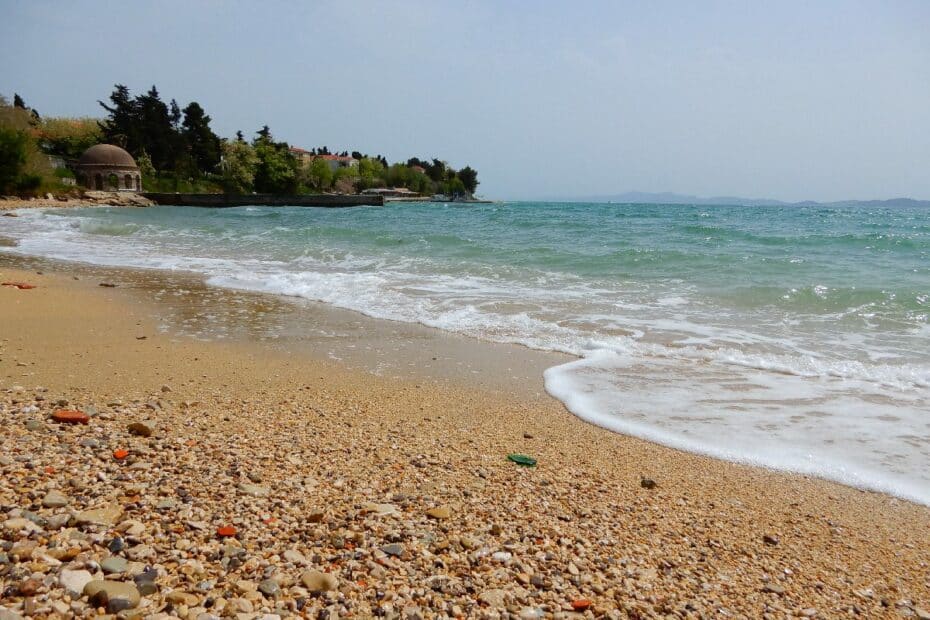 Strand mit Kieselsteinen und sanften Wellen, die an den Uferbereich schlagen.