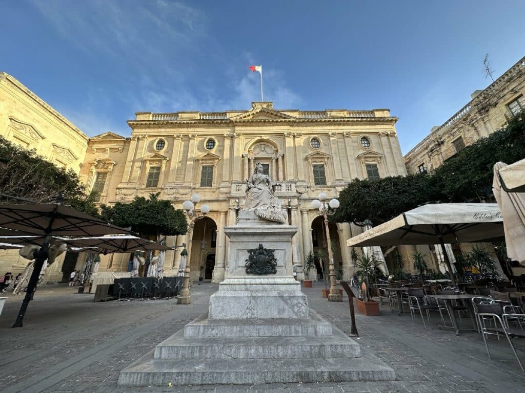Statue auf einem Sockel vor einem historischen Gebäude mit einer Flagge auf dem Dach in Valletta.