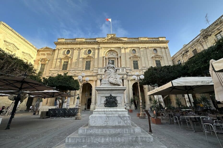 Statue auf einem Sockel vor einem historischen Gebäude mit einer Flagge auf dem Dach in Valletta.