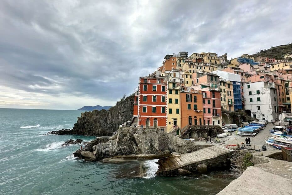 Bunte Gebäude am Wasser in Cinque Terre mit Wolken am Himmel und Booten im Vordergrund.