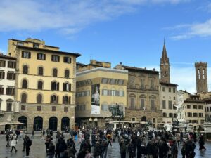 Belebter Platz in Florenz mit historischen Gebäuden und vielen Menschen, darunter ein großer Reiterstandbild.