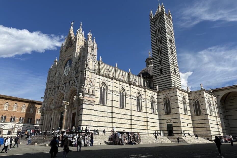 Die Kathedrale von Siena mit ihrer beeindruckenden Fassade und dem hohen Campanile im Hintergrund unter blauem Himmel.