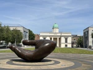 Bronzeskulptur einer großen Hand auf einem Platz in einer städtischen Umgebung.