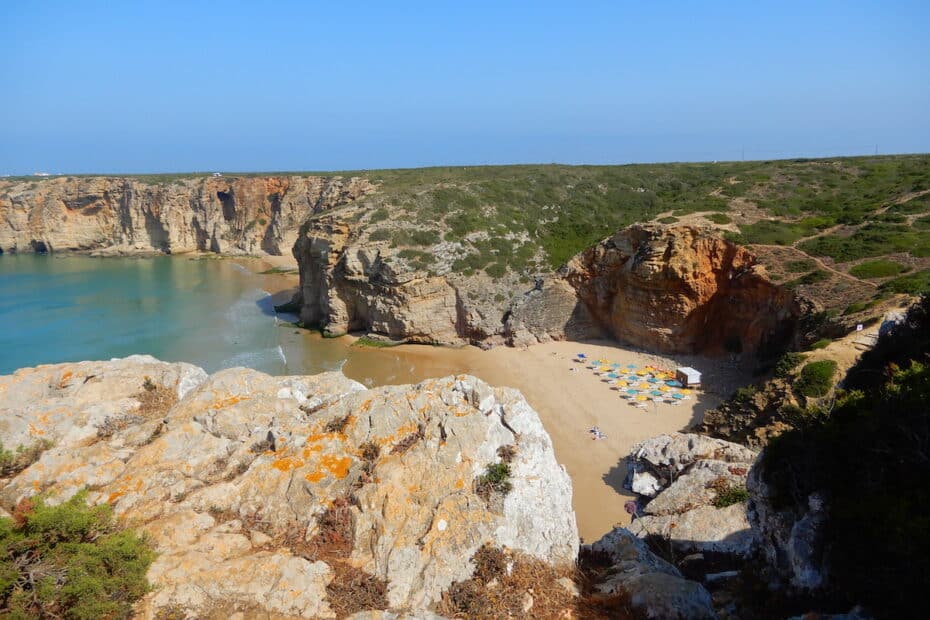 Blick auf eine Küstenlandschaft mit einem kleinen Strand und Klippen im Hintergrund.