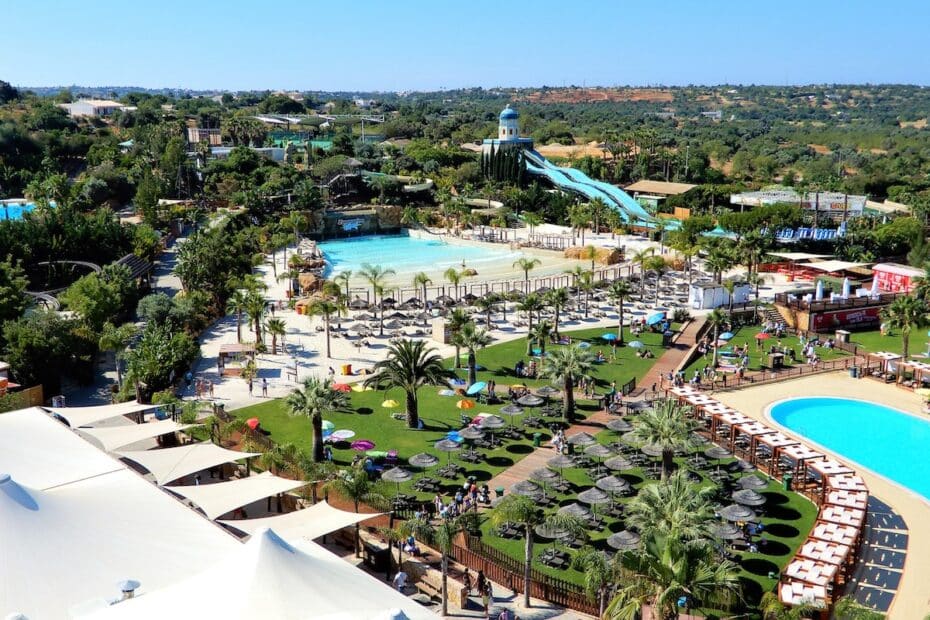 Blick auf einen Wasserpark mit mehreren Pools, Rutschen und Liegen unter Sonnenschirmen.