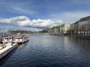 Blick auf die Alster in Hamburg mit mehreren Booten im Wasser und Gebäuden am Ufer.