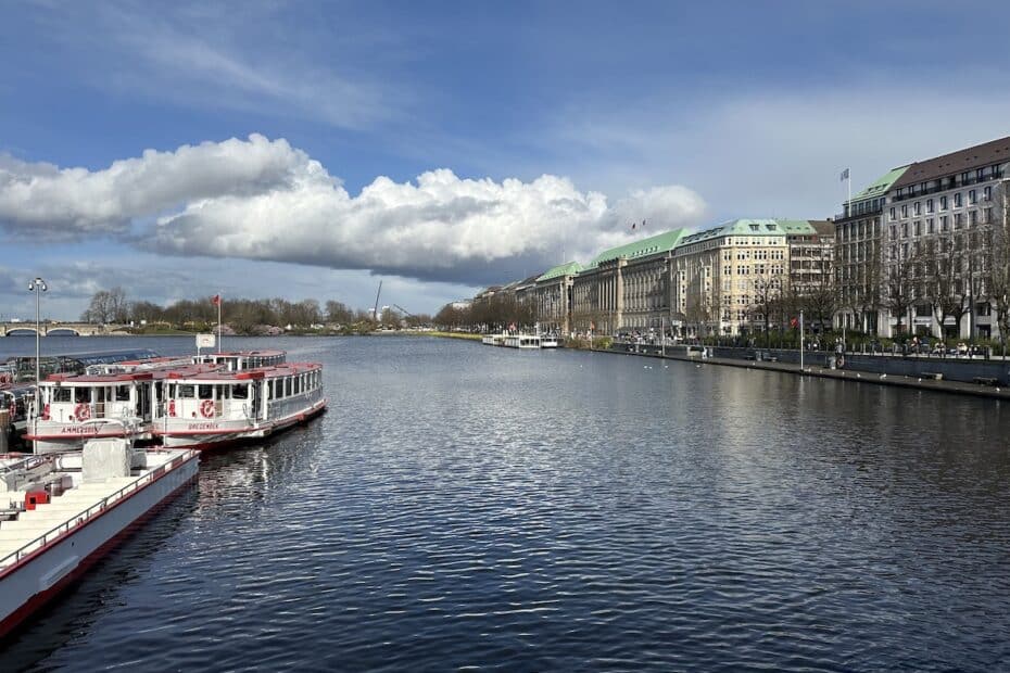 Blick auf die Alster in Hamburg mit mehreren Booten im Wasser und Gebäuden am Ufer.