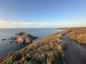 Küstenlandschaft mit Felsen, Meer und einem Wanderweg entlang der Küste bei klarem Himmel.