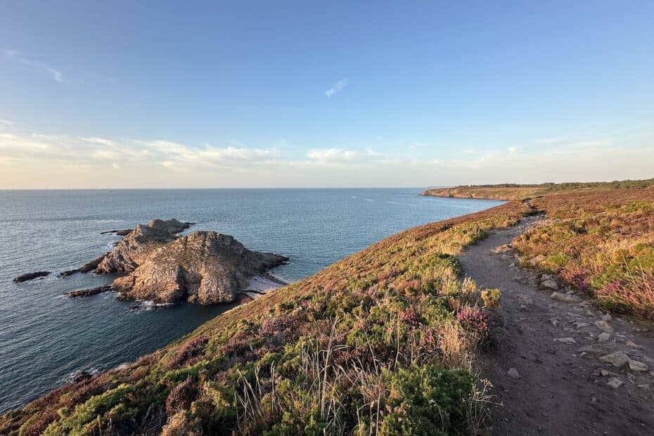 Küstenlandschaft mit Felsen, Meer und einem Wanderweg entlang der Küste bei klarem Himmel.