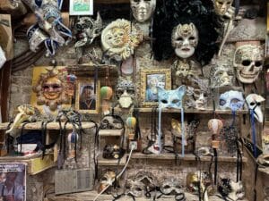 Eine Sammlung von verschiedenen Masken, darunter venezianische und dekorative Modelle, an einer Wand in einem Geschäft.