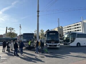 Mehrere Busse an einem Busbahnhof mit Reisenden, die mit Gepäck unterwegs sind.
