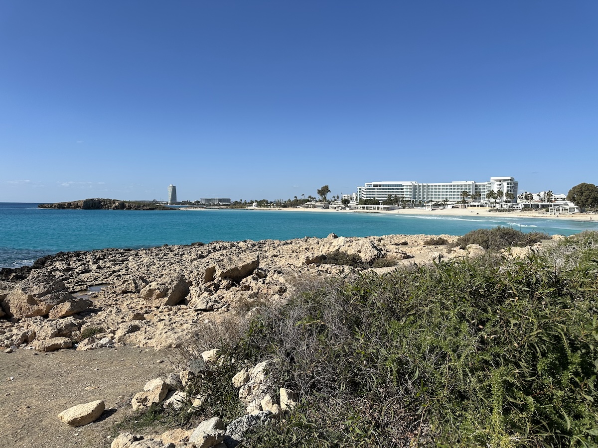 Türkises Meer an einer felsigen Küste bei Ayia Napa mit Hotelanlage und Promenade auf Zypern unter klarem Himmel