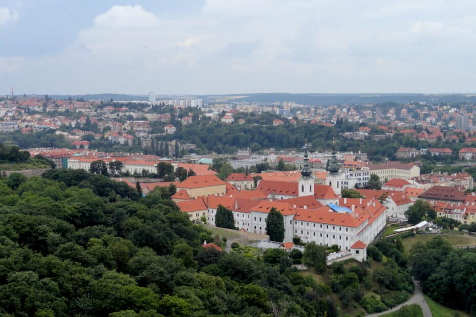 Luftaufnahme eines historischen Gebäudes mit roten Dächern und umgebenden Bäumen in einer städtischen Landschaft.