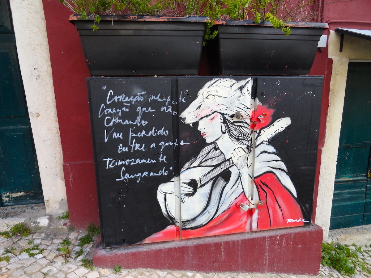 Wandmalerei zeigt eine Frau mit Gitarre, die eine Wolfsmasken trägt, mit Text auf der Wand.