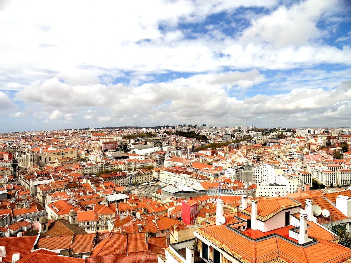 Blick auf die Stadt Lissabon mit vielen roten Dächern und einem bewölkten Himmel.