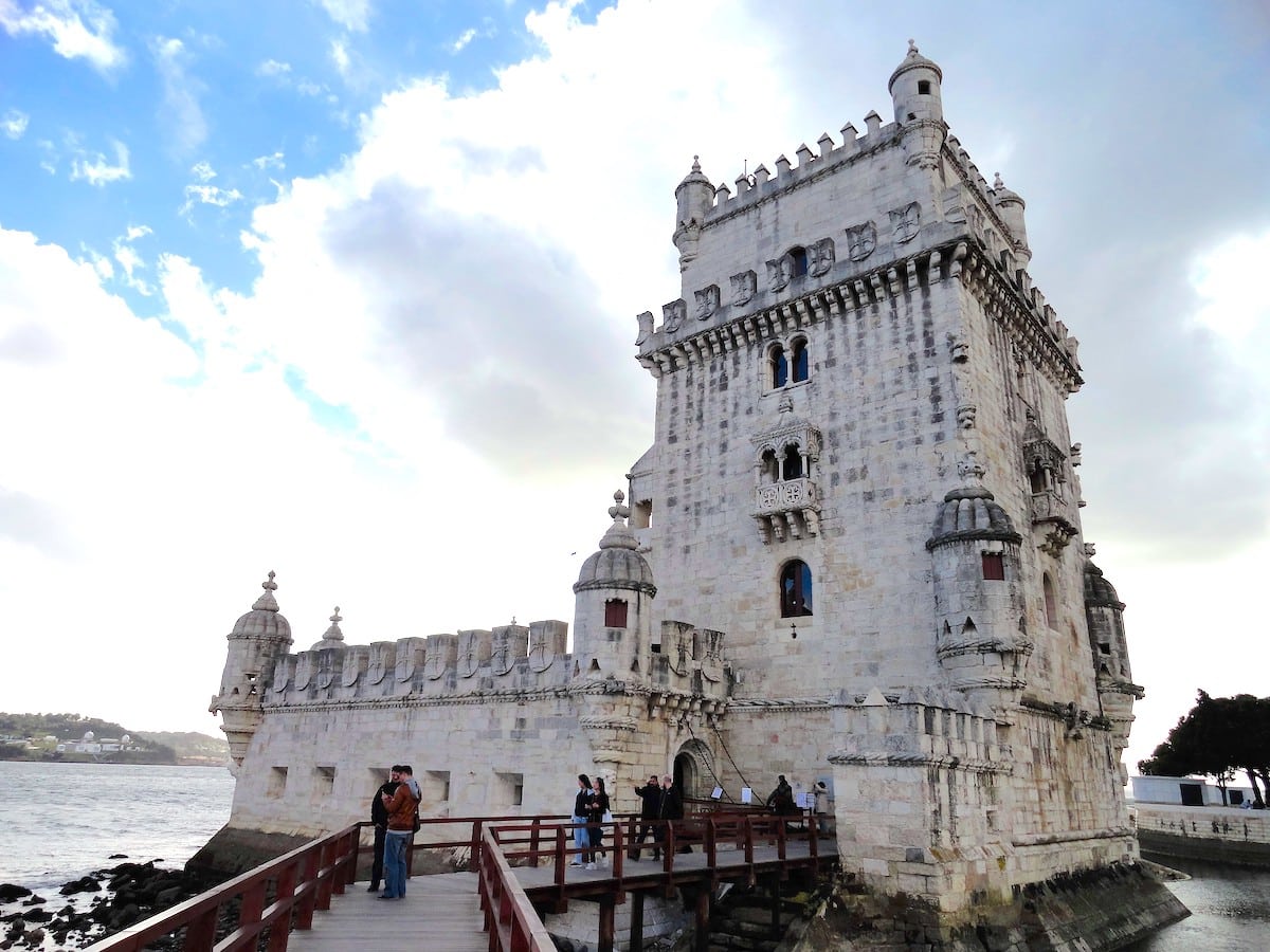 Historisches Gebäude Torre de Belém in Lissabon mit steinernen Details und Menschen auf der Brücke.