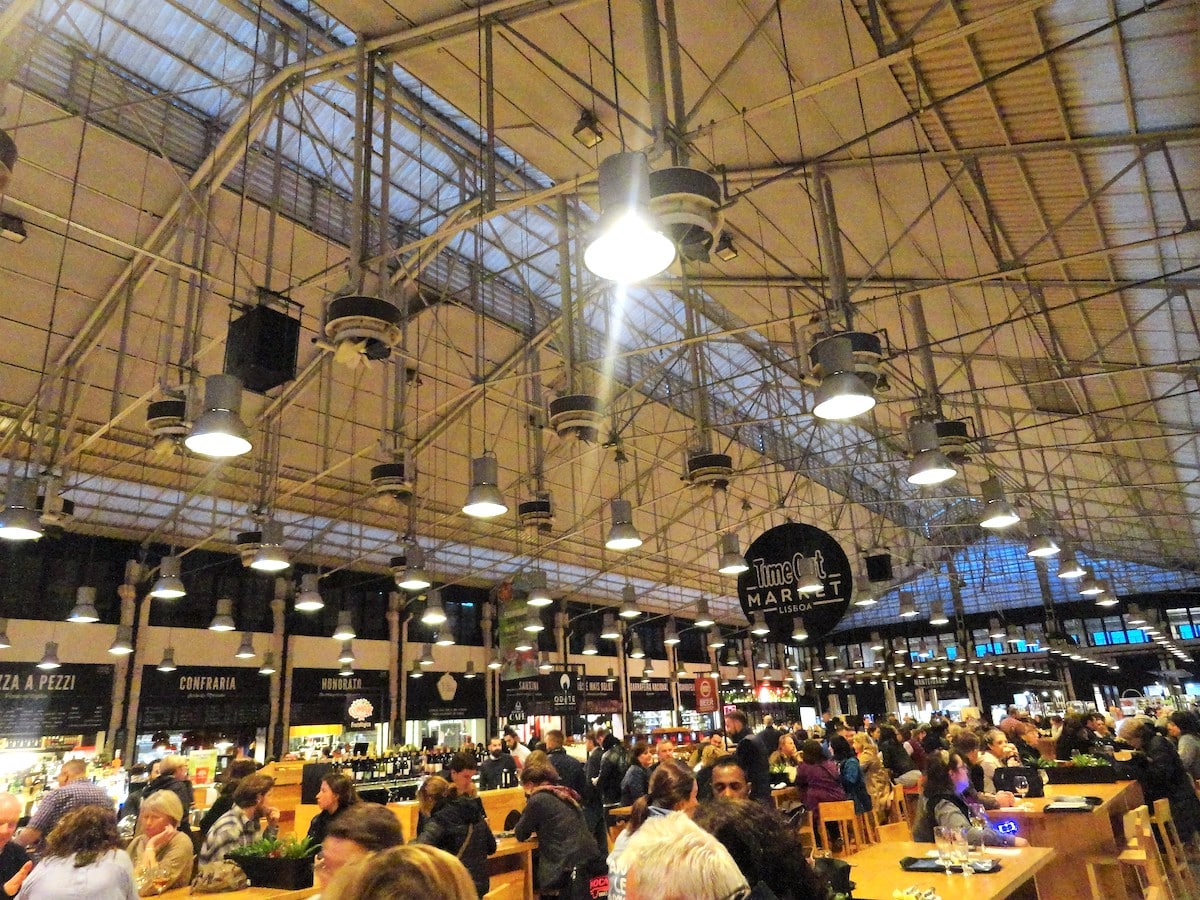 Innenansicht einer Markthalle mit vielen Menschen und einer hohen Decke mit Beleuchtung.