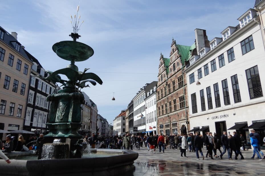 Brunnen mit Wasserspiel auf einem Platz in Kopenhagen, umgeben von Gebäuden und Menschen.